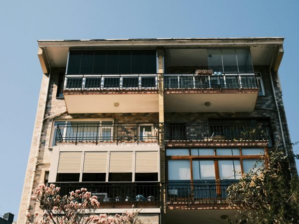 A modern apartment building facade with blooming flowers in the foreground under a clear blue sky.